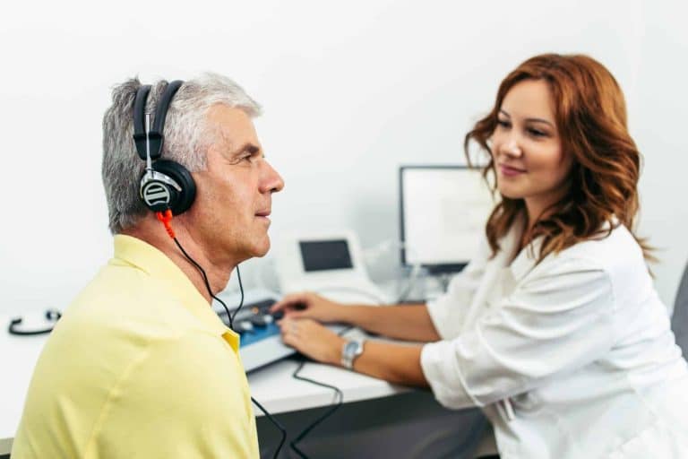 Man in a hearing care professionals office with headphones on listening intently during a hearing test